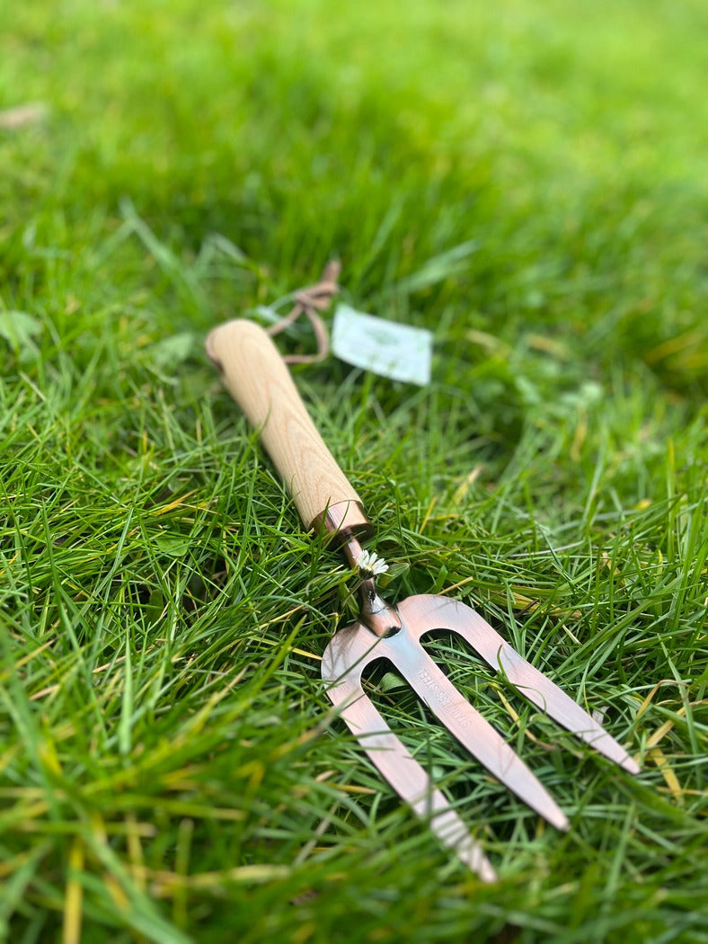Flot havegaffel med træhåndtag og kobberbelægning, der ligger på en græsplane