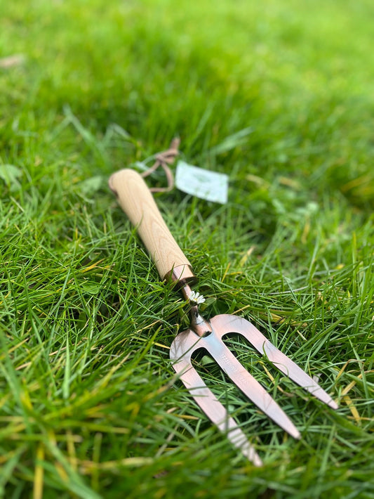 Flot havegaffel med træhåndtag og kobberbelægning, der ligger på en græsplane