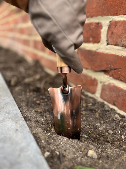 Fin planteskovl med træhåndtag og kobberbelagt skæft, der graver i jorden