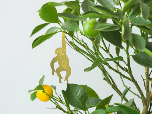 Lille Chimpanse figur i messing, der hænger i en plante