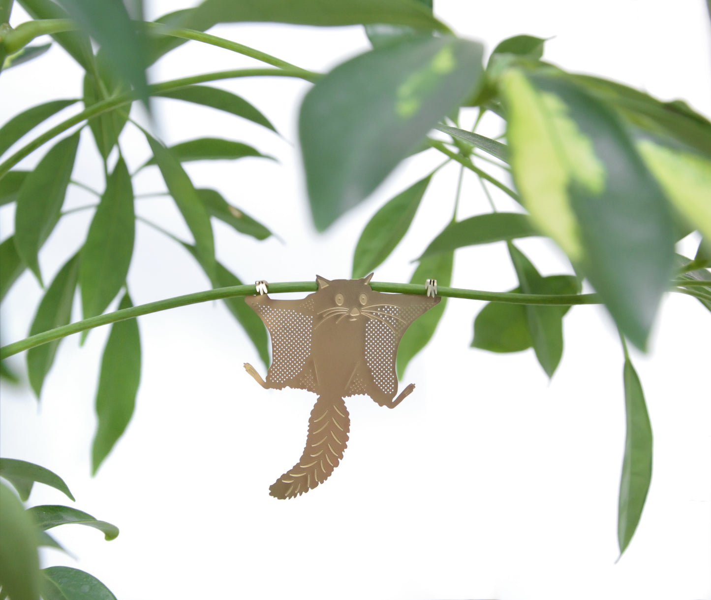 Messingfigur af flyveegern hængende i en plantestængel
