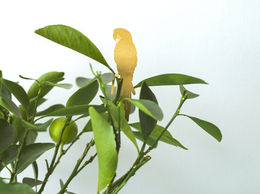 Lille papegøje figur i messing, der sidder i en grøn plante