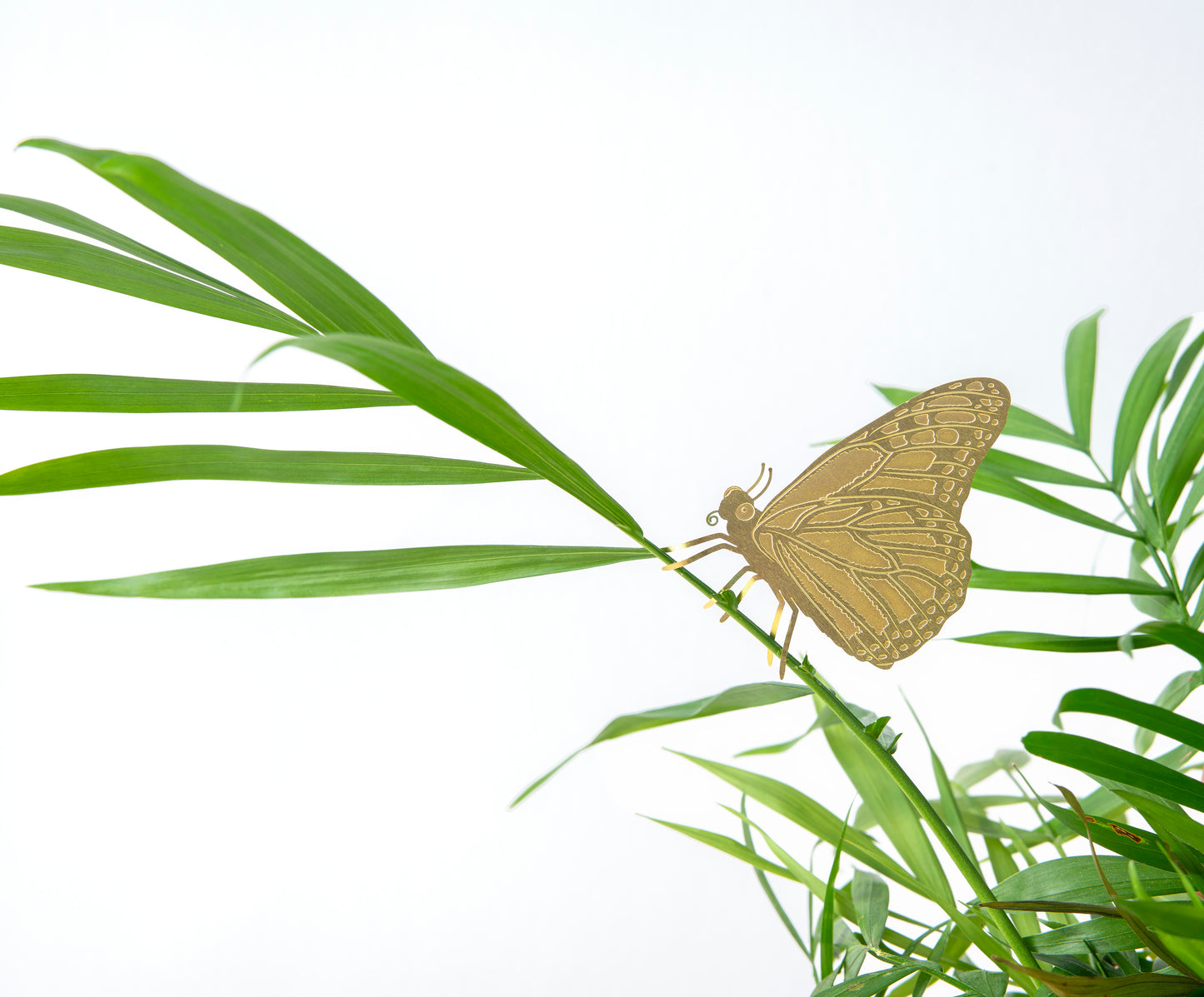 Messinge figur af en sommerfugl, der sidder i en plante